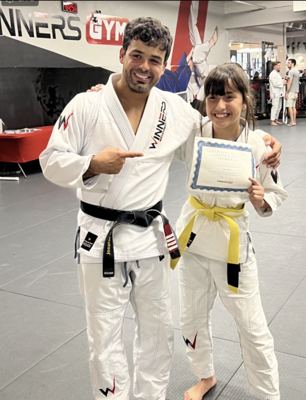 Jade Ghezal receiving her belt promotion from Coach Jonatas Gurgel at Winners Jiu-Jitsu Academy